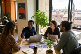 Entrepreneurs in a modern coworking space in Occitanie, exchanging business cards and discussing around a wooden table in natural light, with a view of Toulouse rooftops.