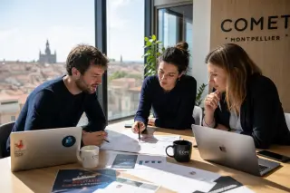 Entrepreneurs discussing a business plan in a sunlit Occitanie coworking space, with laptops and documents on the table.