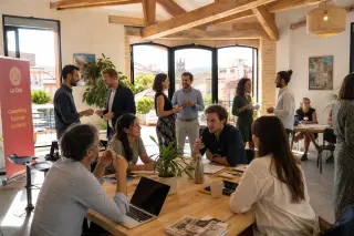 Coworking space in southern France with entrepreneurs in small groups, exchanging business cards and discussing projects in natural morning light.