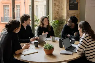 Coworking space in southern France with a small group of entrepreneurs having a focused discussion at a table, natural warm light and muted urban tones.