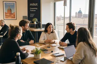 Coworking space in Occitanie with entrepreneurs networking around a sunlit table, French urban hints in the background.